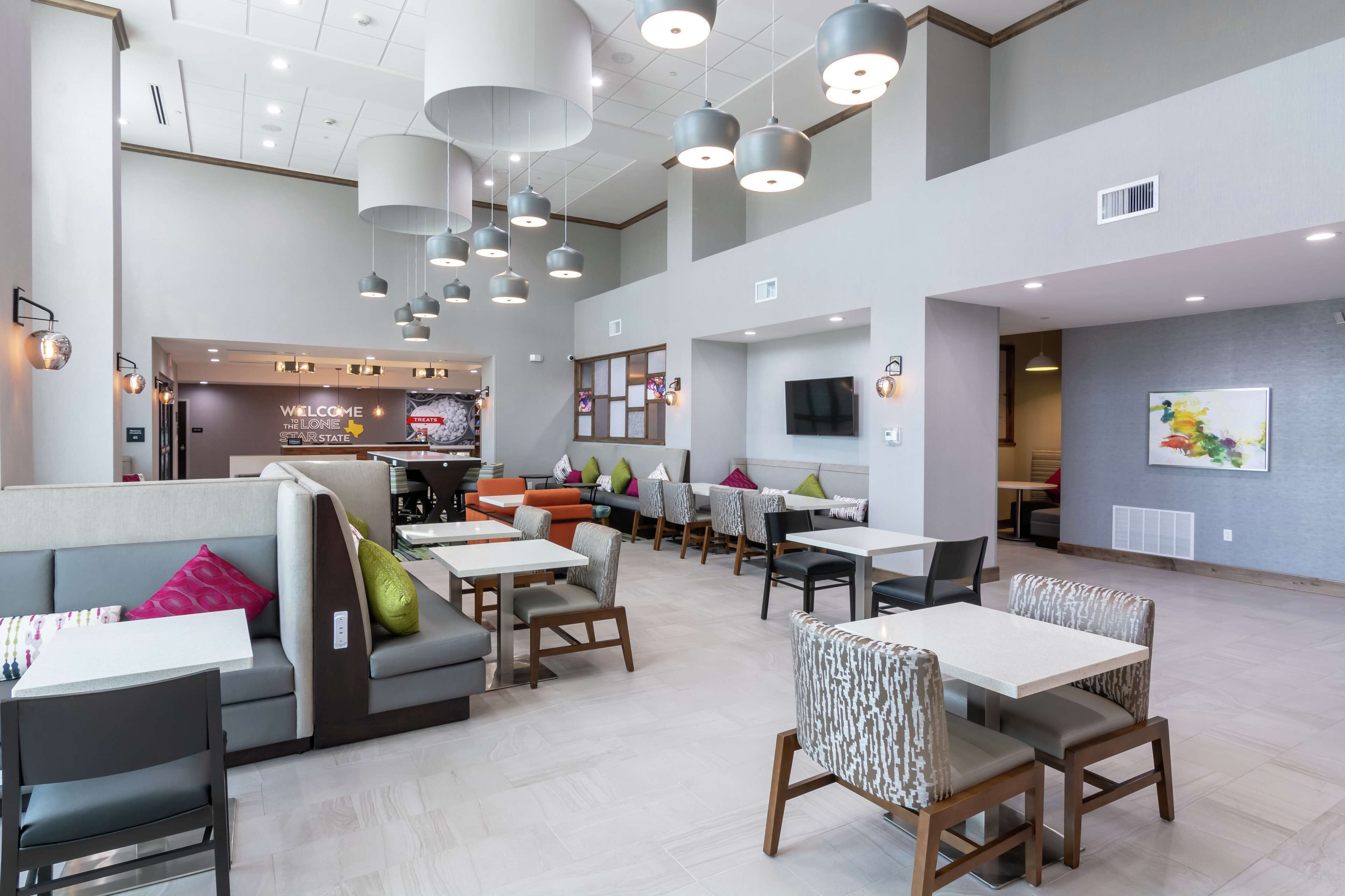 Un amplio vestíbulo de hotel con varias zonas de estar, incluyendo sofás y mesas, y un mostrador de recepción al fondo.