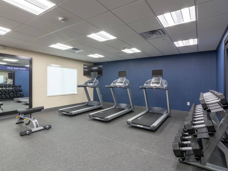 Un gimnasio con cintas de correr, mancuernas y un espejo.