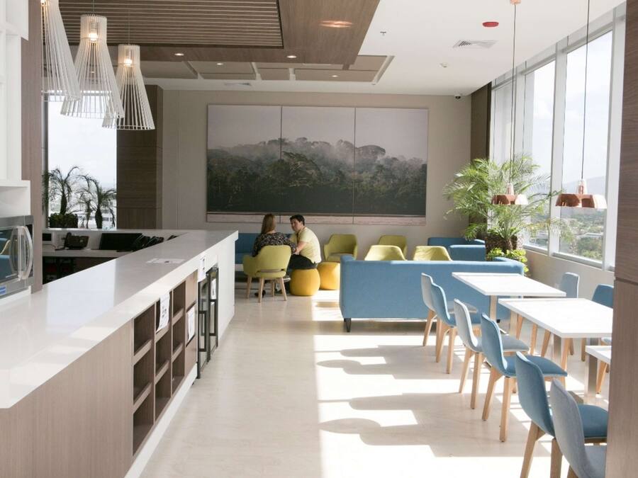 Cocina moderna con una isla central, zona de estar con sillas amarillas y azules, y un amplio ventanal con vistas a la ciudad.