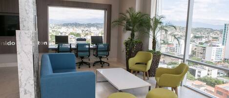 A modern living room with a city view, featuring a sofa, chairs, a coffee table, and a large window.