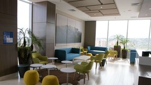 A modern lounge area with a blue sofa, yellow and green chairs, and small tables.
