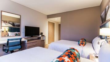 A hotel room with two beds, a desk with a computer, a television, and a mirror.