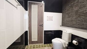 A bathroom with a toilet, a trash bin, a towel, and a door.