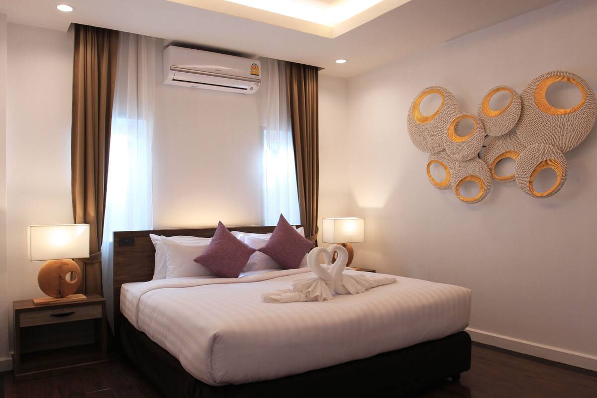 Una habitación de hotel con una cama grande, dos mesitas de noche con lámparas, un equipo de aire acondicionado y un adorno en la pared.