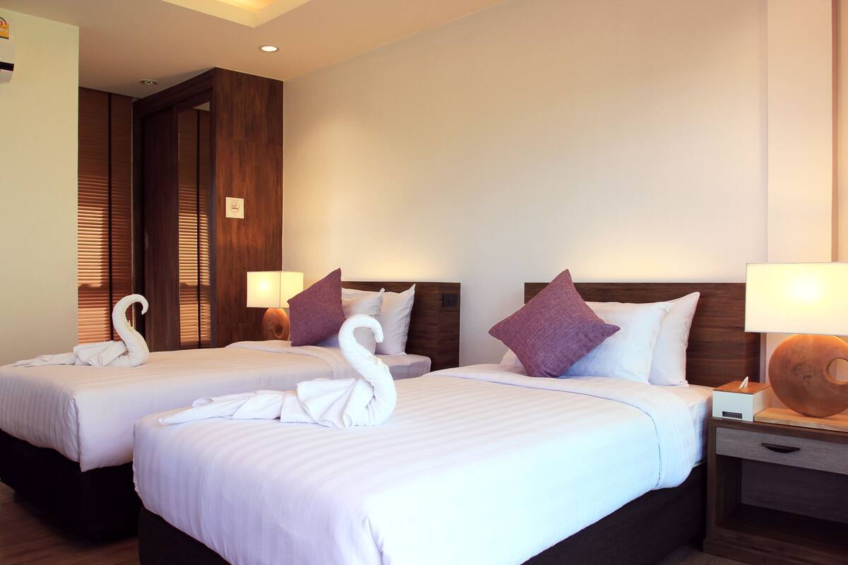 Habitación de hotel con dos camas, cada una con una toalla con forma de cisne, cabeceros de madera y lámparas de noche.