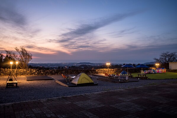 A campsite at dusk with a tent, seating, and a view of the landscape.