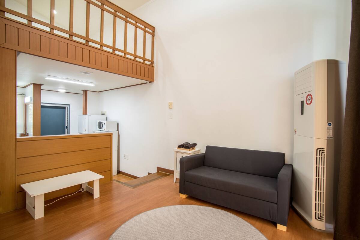 Un espacio habitable compacto con sofá, una mesita, un banco, kitchenette y calefacción integrada.