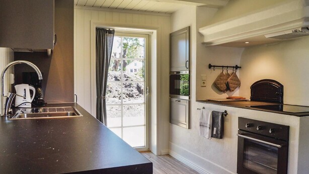 A modern kitchen with a large island, built-in oven, and a window with curtains. - Cozy home in Herräng with WiFi (Herräng)
