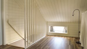 A room with wooden floors, white walls, a window with curtains, and a black floor lamp. - Cozy home in Herräng with WiFi (Herräng)