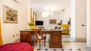 Habitación de hotel con un escritorio de madera, una silla, una cama con cubierta roja, un televisor y obras de arte en las paredes.