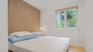 A bedroom with a bed, a window with a view of greenery, and a wall with vertical wooden slats.