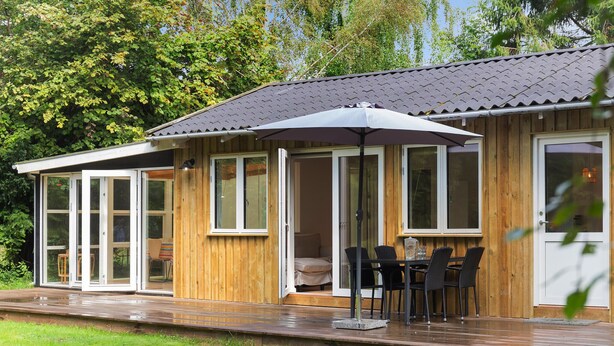 A wooden house with a covered patio, glass doors, and a table with chairs.