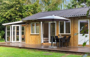 A wooden house with a covered patio, glass doors, and a table with chairs.