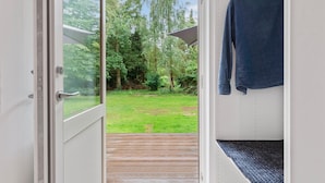 A door leading to a wooden deck with a view of a grassy yard and trees.