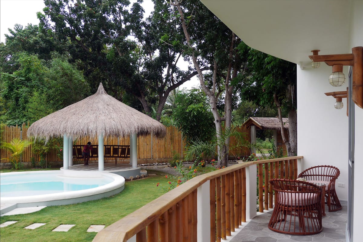 Un área de piscina con una estructura de techo de paja, sillas de madera y una valla de bambú.