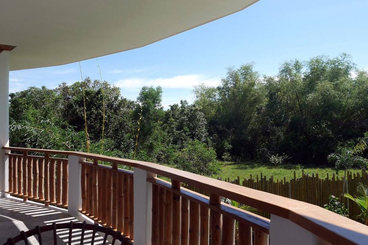 Un balcón con baranda de madera que da a un paisaje verde exuberante y un cielo azul despejado.