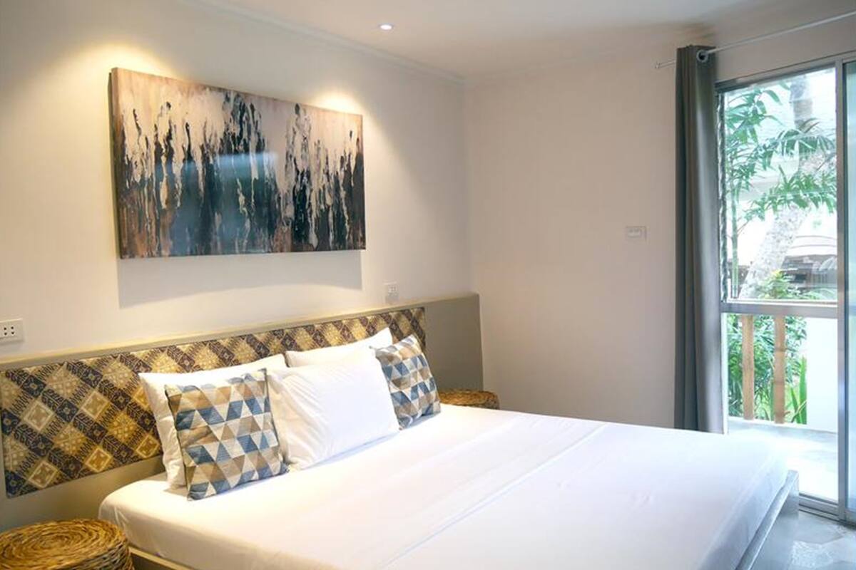 Un dormitorio con una cama grande, cabecera con diseños estampados, una obra de arte colgada en la pared y una ventana con vistas al verdor.