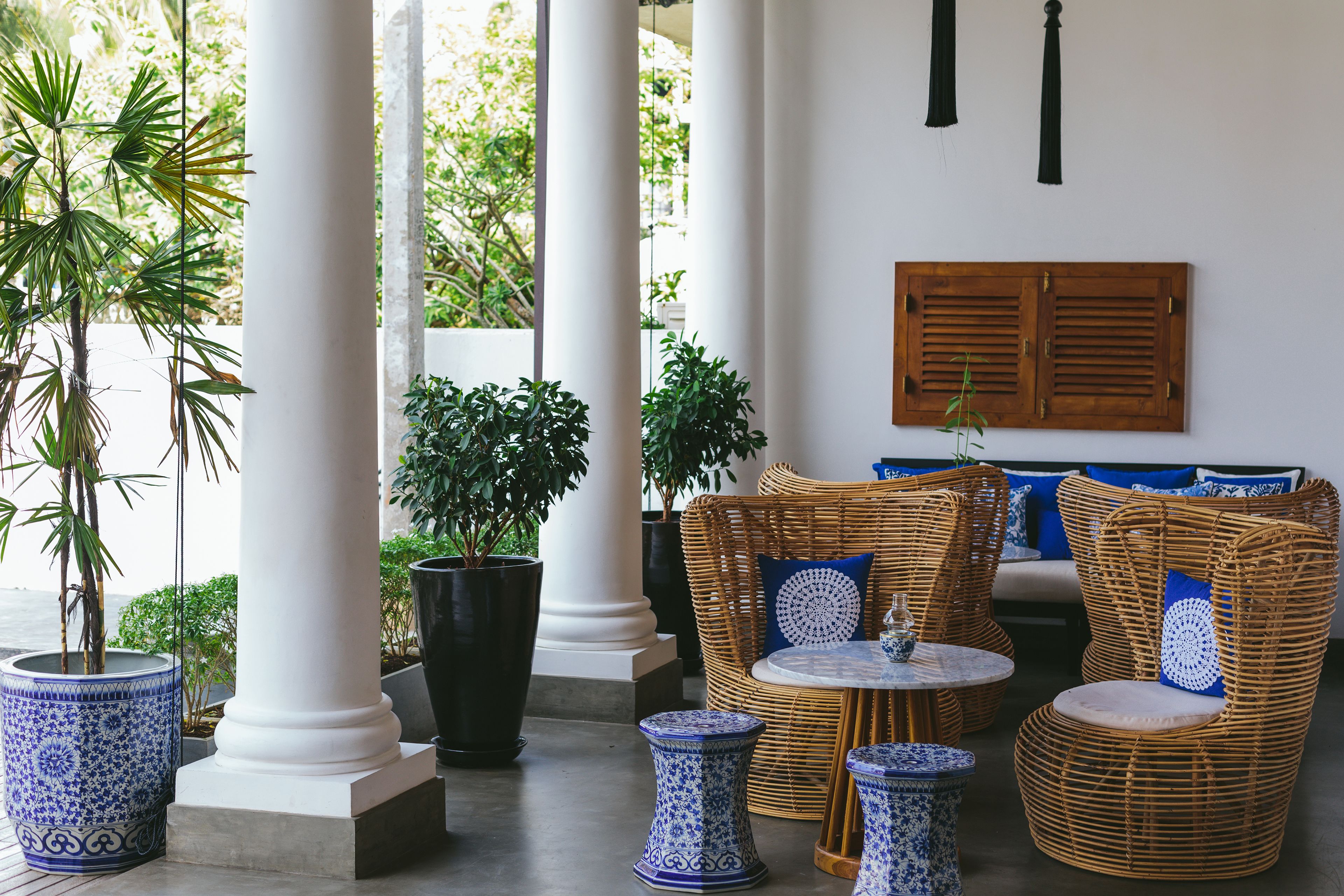 A covered outdoor seating area with wicker furniture, potted plants, and a wooden shutter wall.