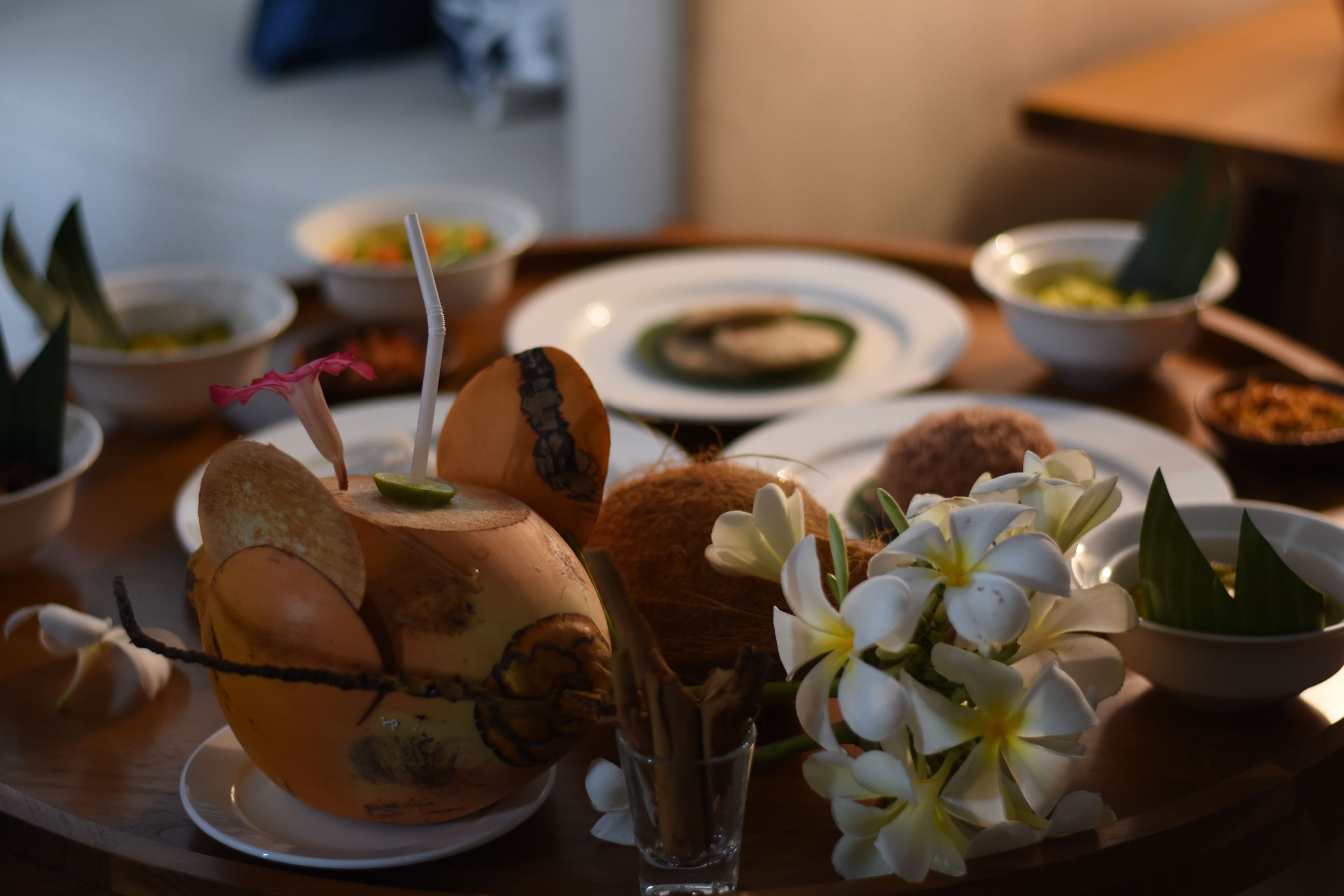 A dining table with various dishes, including a coconut and a glass of water, surrounded by flowers and a small bowl.