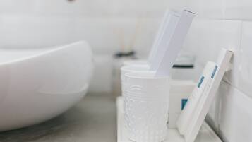 A white bathroom with a white sink, a white cup holder with a cup and a toothbrush, and a white soap dispenser.