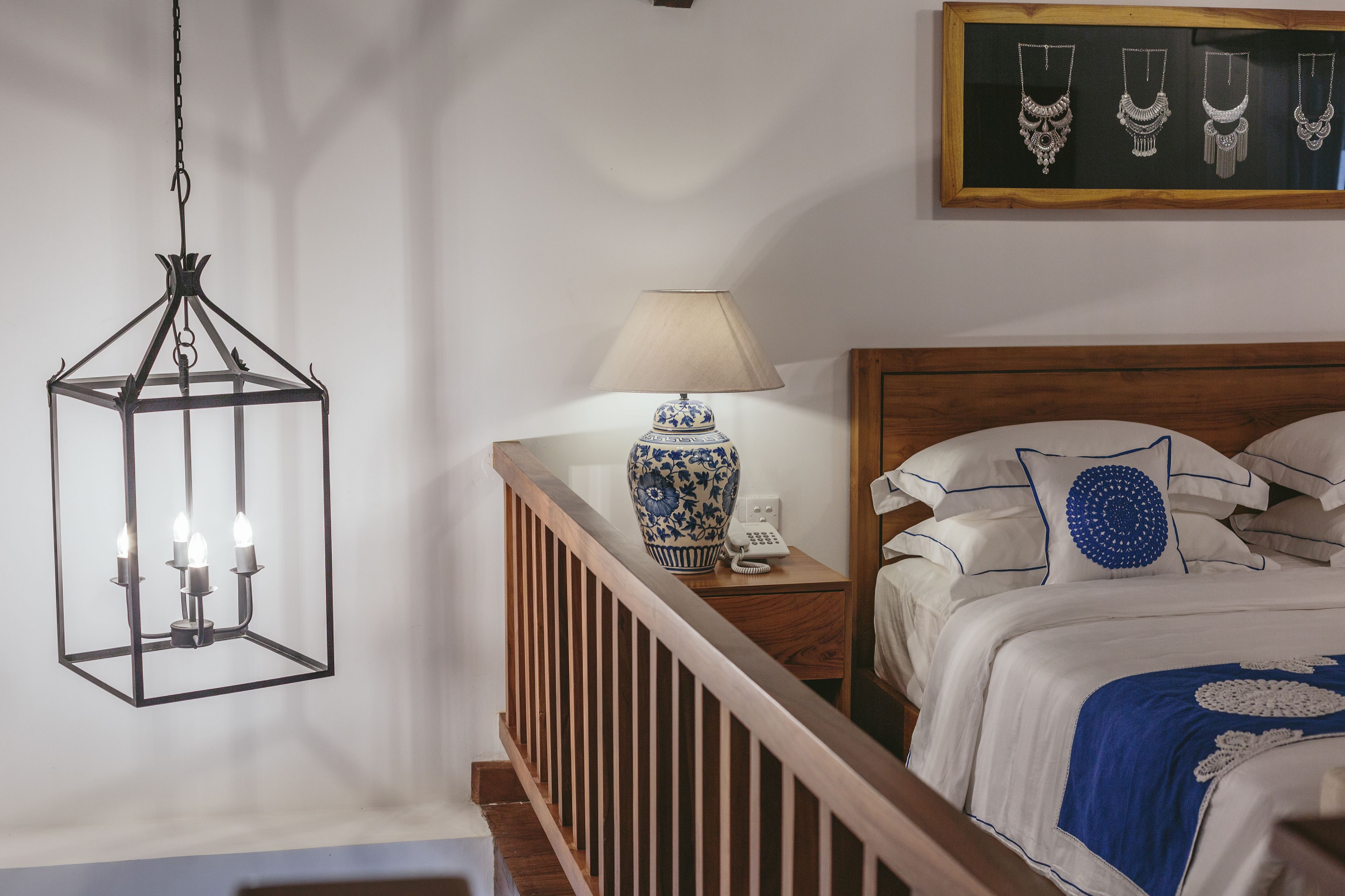 A bedroom with a wooden headboard, a bedside table with a lamp, and a hanging light fixture.