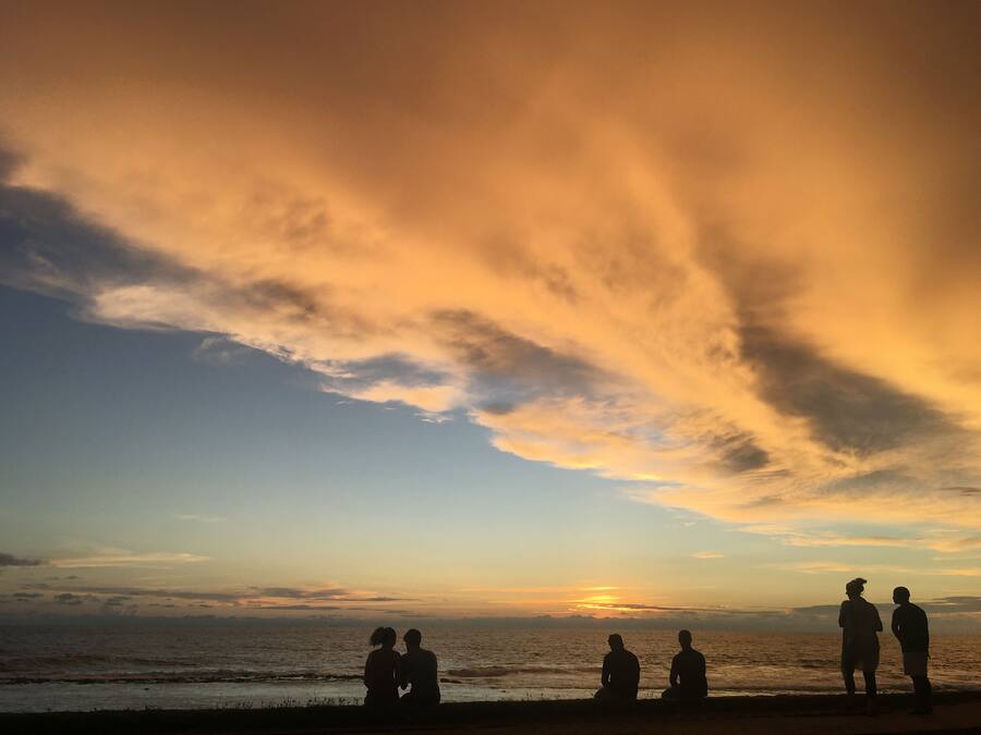 Ein Sonnenuntergang über dem Meer mit Silhouetten von Menschen am Strand.
