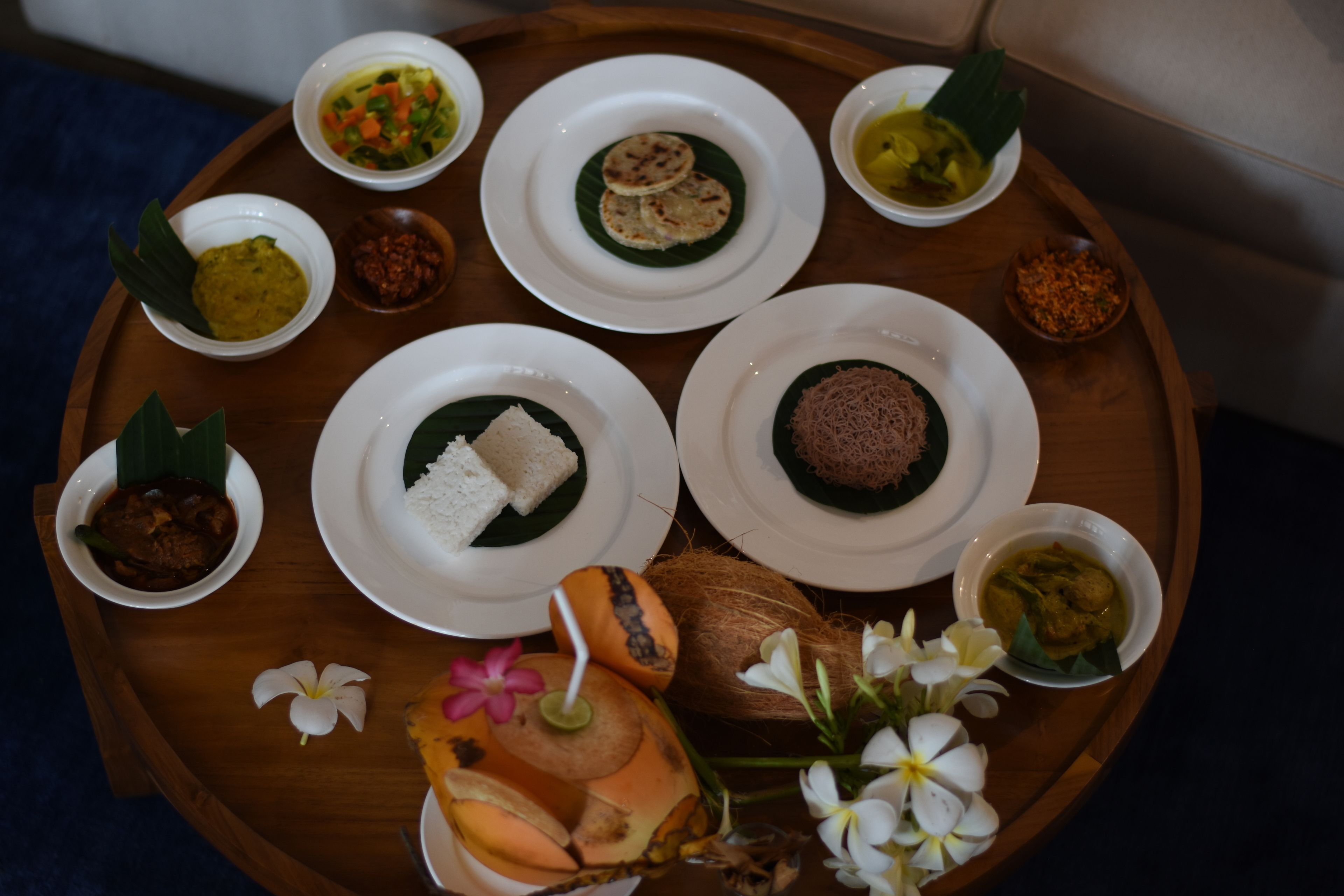 A wooden tray with various dishes, including rice, curries, and a coconut.