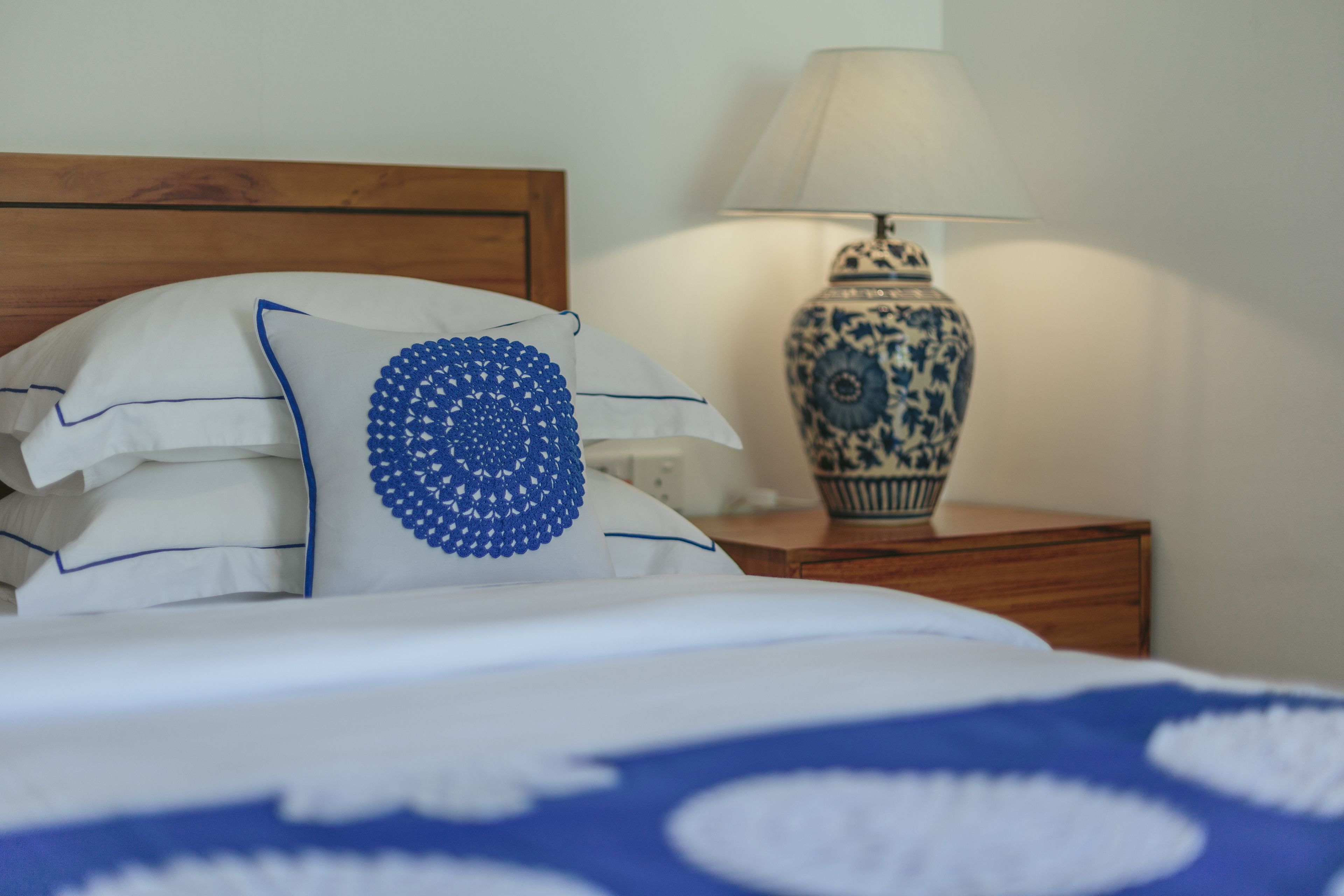 A neatly made bed with white and blue bedding, a blue and white patterned pillow, and a wooden headboard.