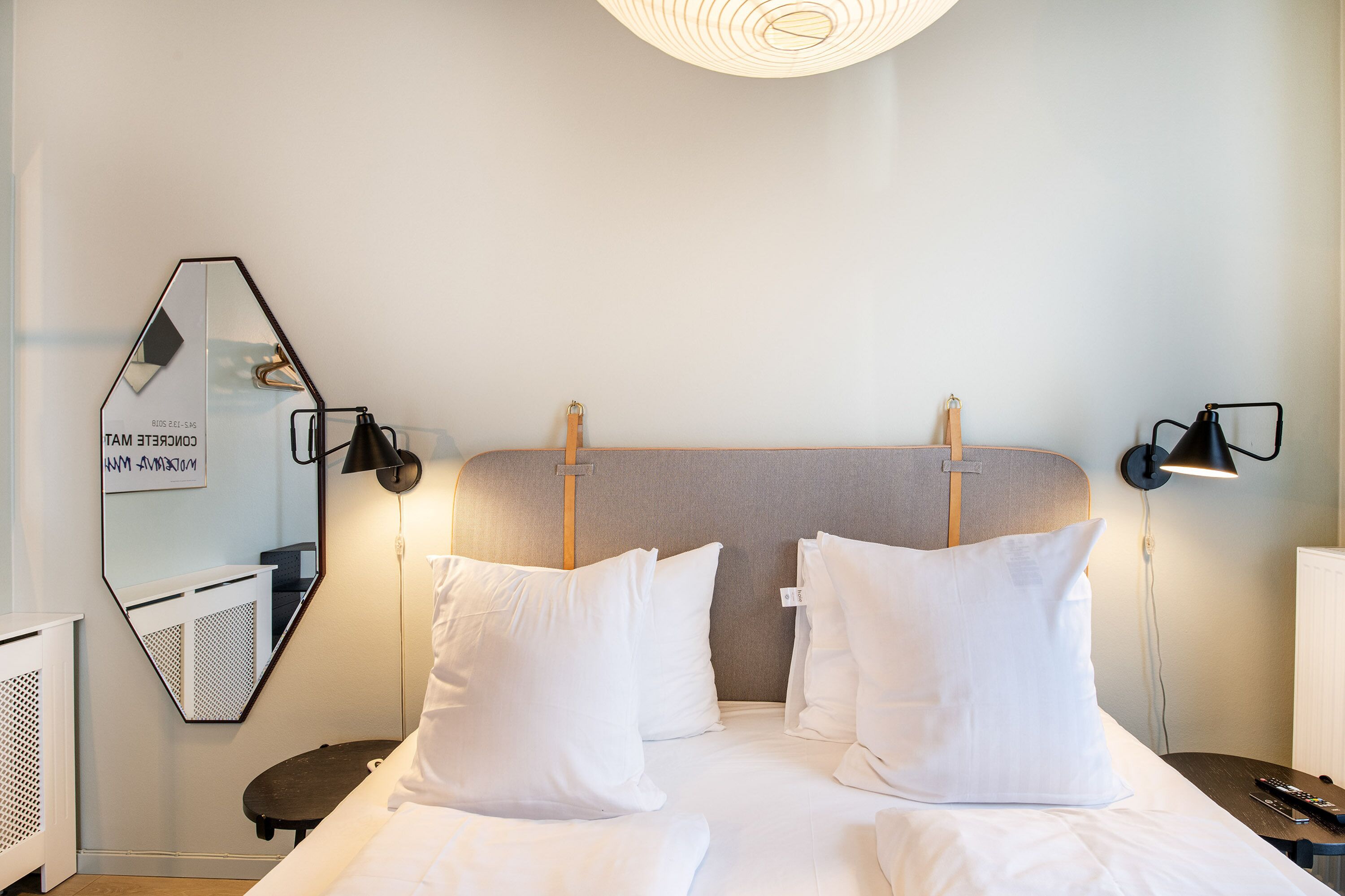 A hotel room with a large bed, two bedside tables, a wall-mounted mirror, and a ceiling light fixture.
