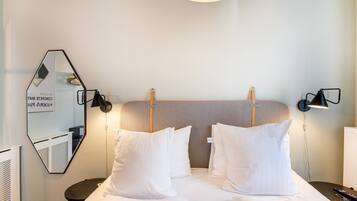 A hotel room with a large bed, two bedside tables, a wall-mounted mirror, and a ceiling light fixture.