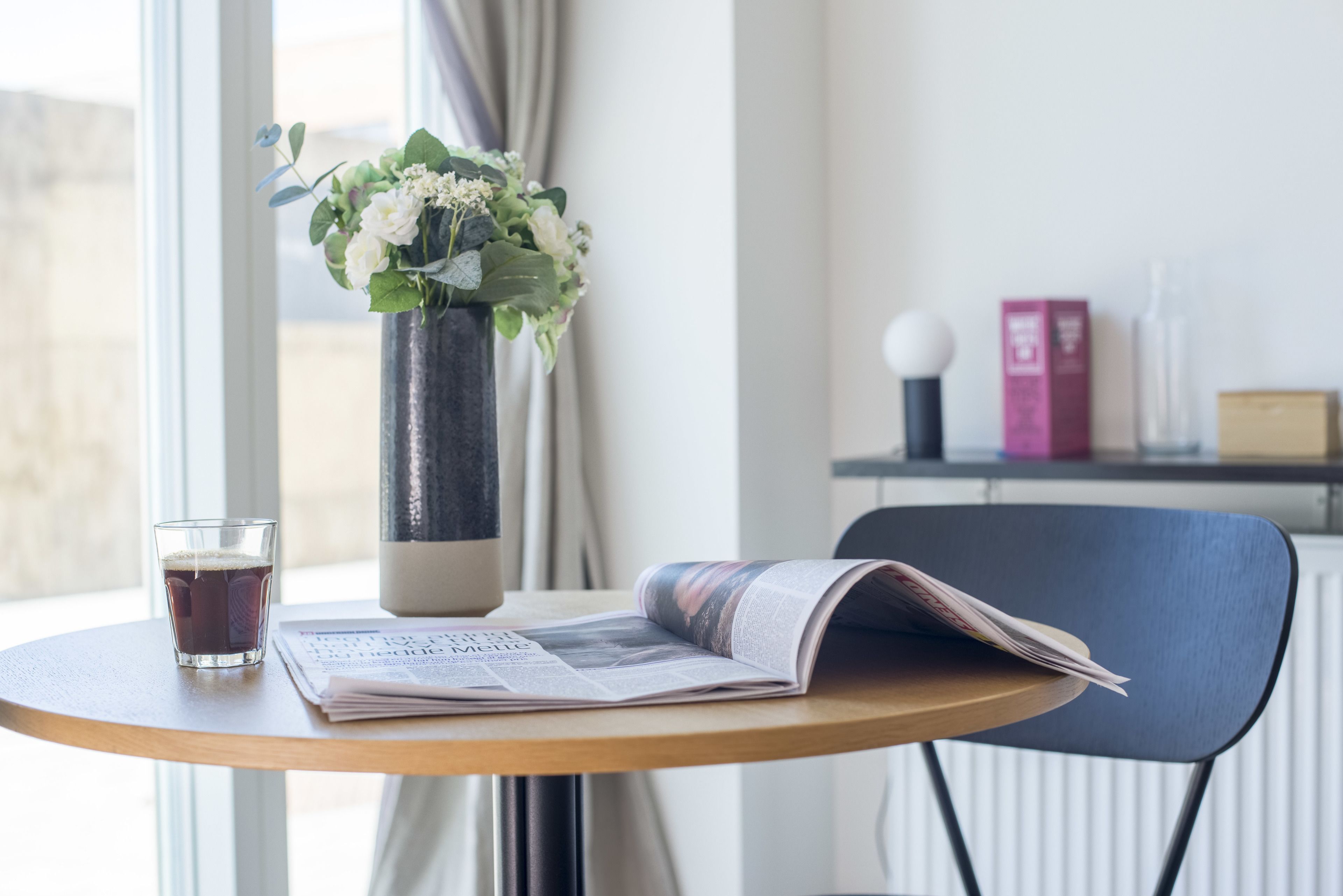 A table with a glass of iced tea, a vase with flowers, and an open magazine.