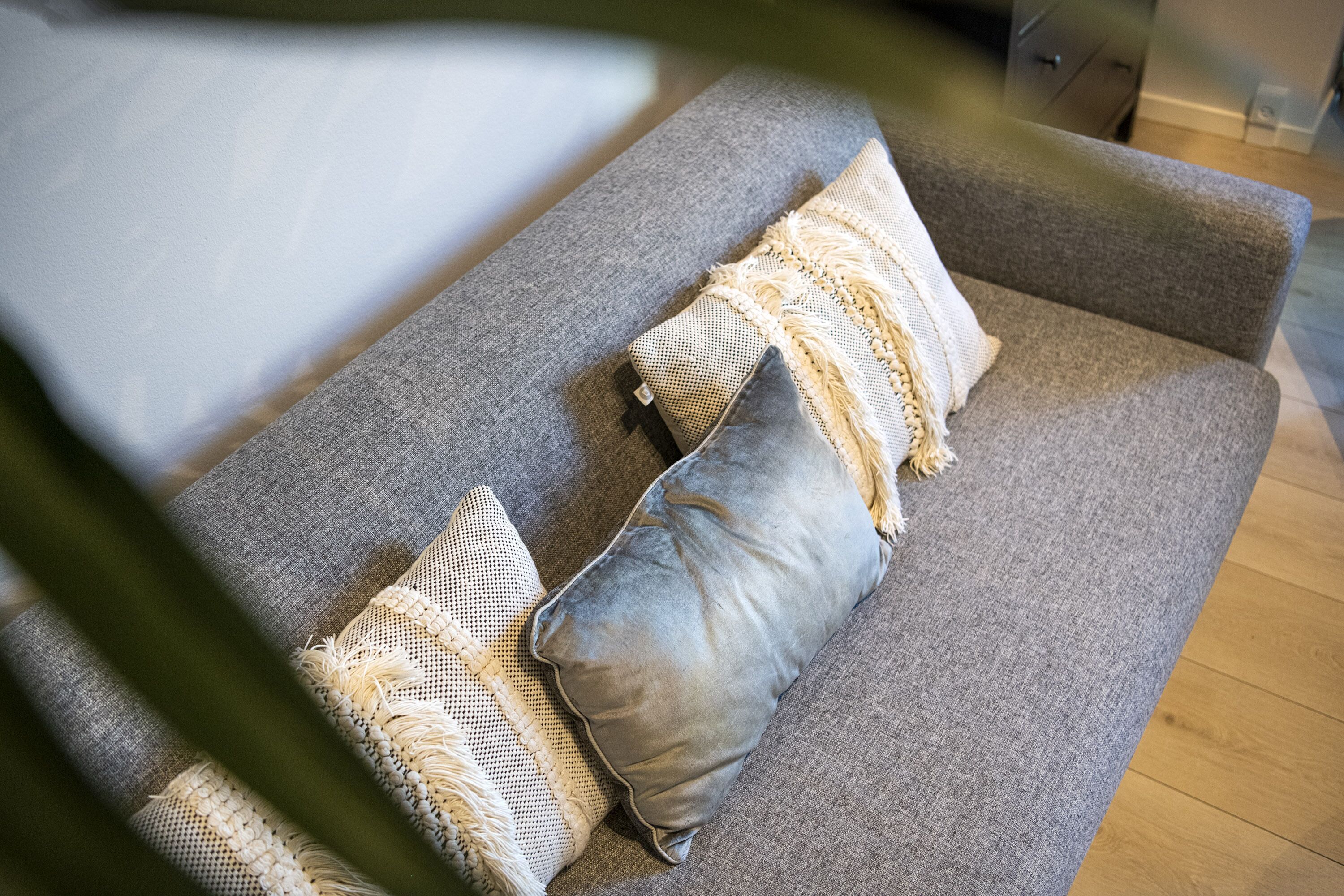 A grey sofa with two textured pillows and a woven throw blanket.