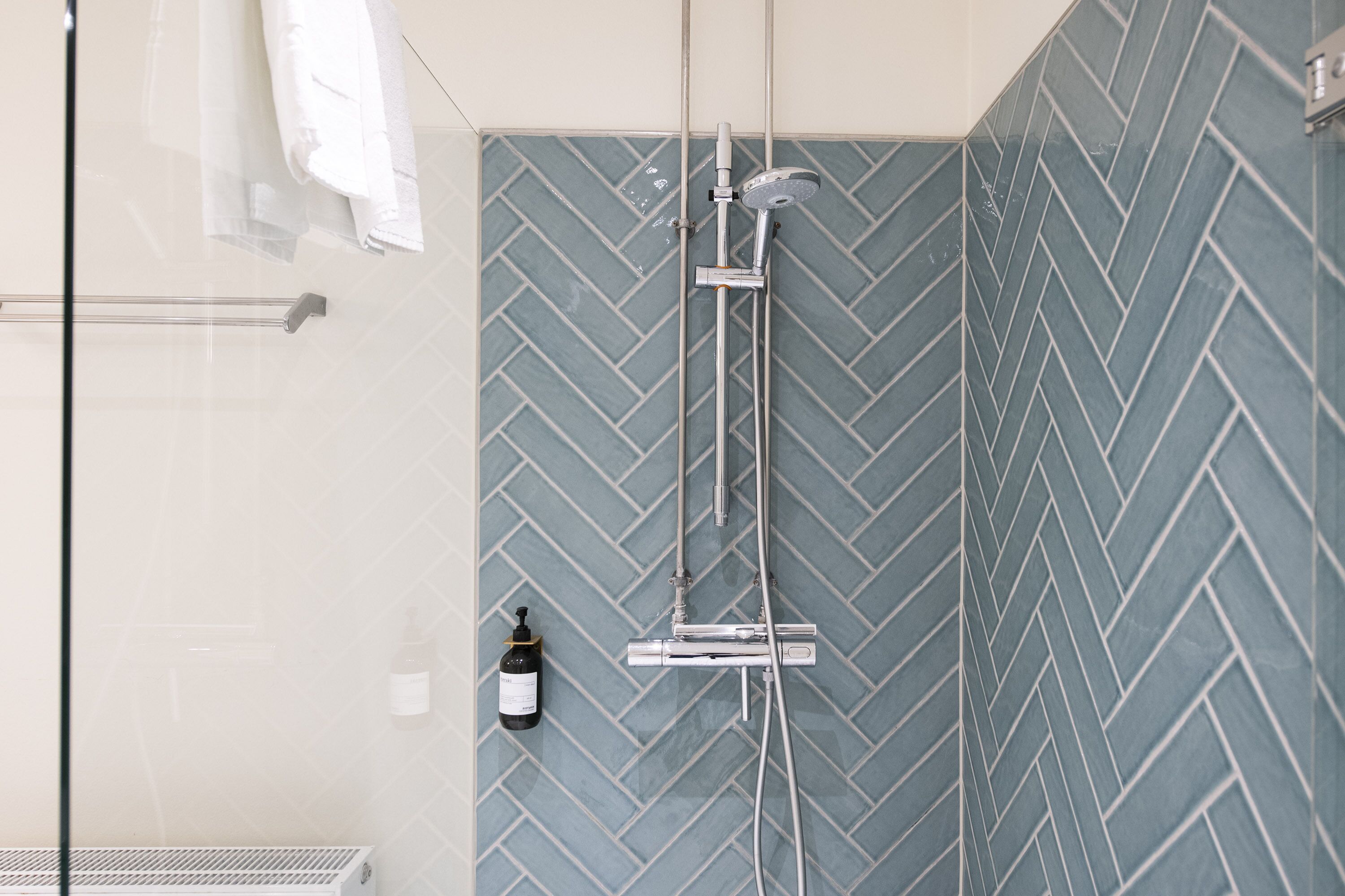 Chuveiro com padrão de azulejos em espinha de peixe, porta-toalhas e uma garrafa de shampoo.