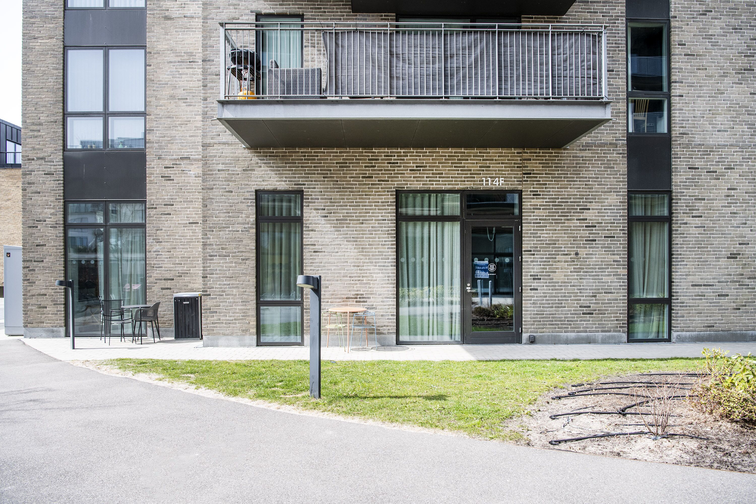 A modern building with a brick facade, large windows, and a balcony with metal railings.