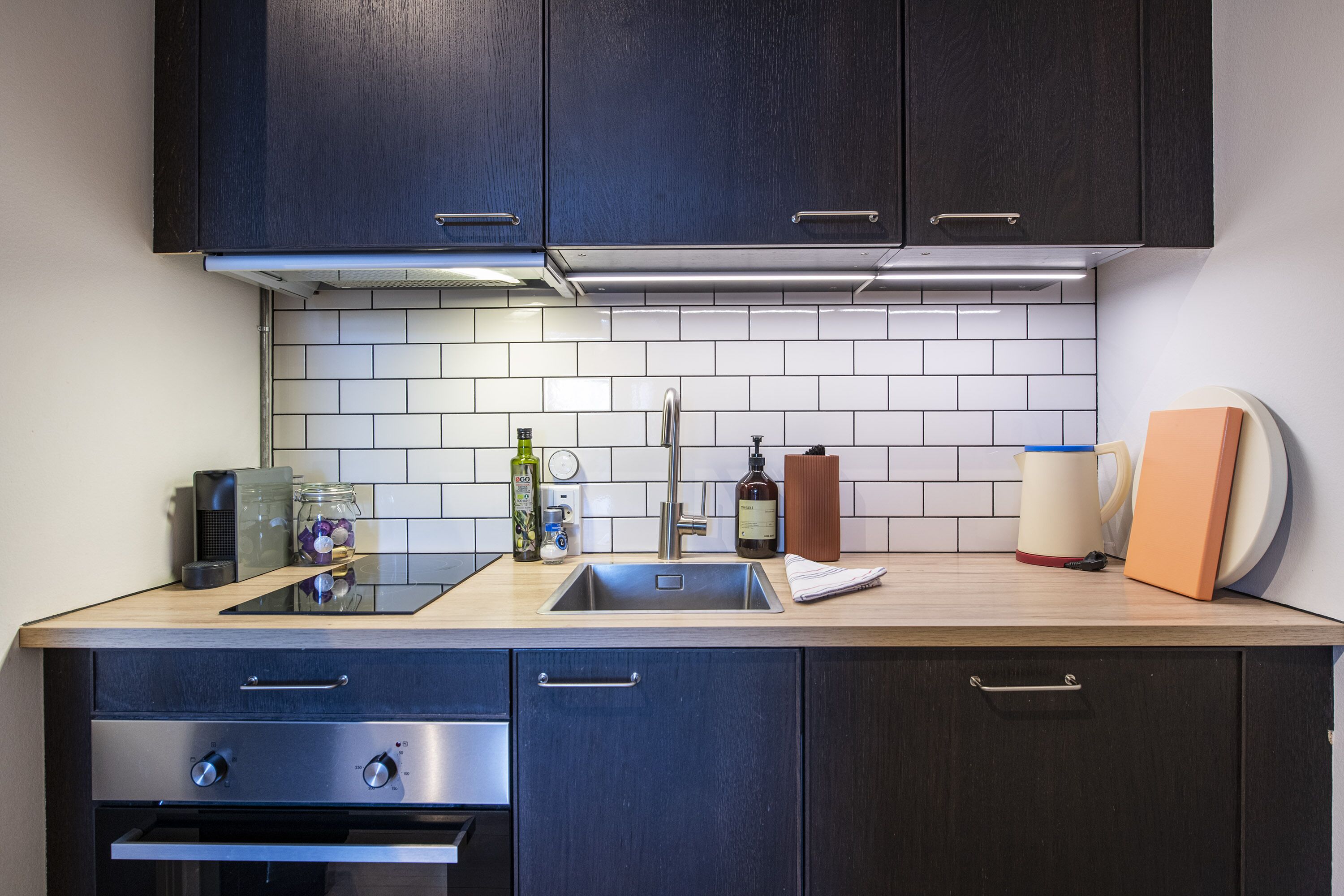 A modern kitchen with dark cabinets, a stainless steel sink, and a wooden countertop.