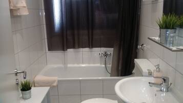 A bathroom with a bathtub, a sink, and a toilet. There is a towel hanging on the wall, a potted plant on the counter, and a shower curtain.