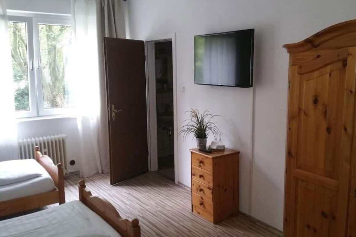 A bedroom with a bed, a wooden wardrobe, a dresser, a television, and a door leading to another room.