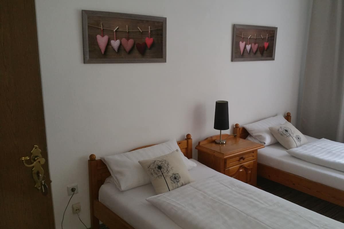A bedroom with two single beds, a bedside table with a lamp, and heart-shaped decorations on the wall.