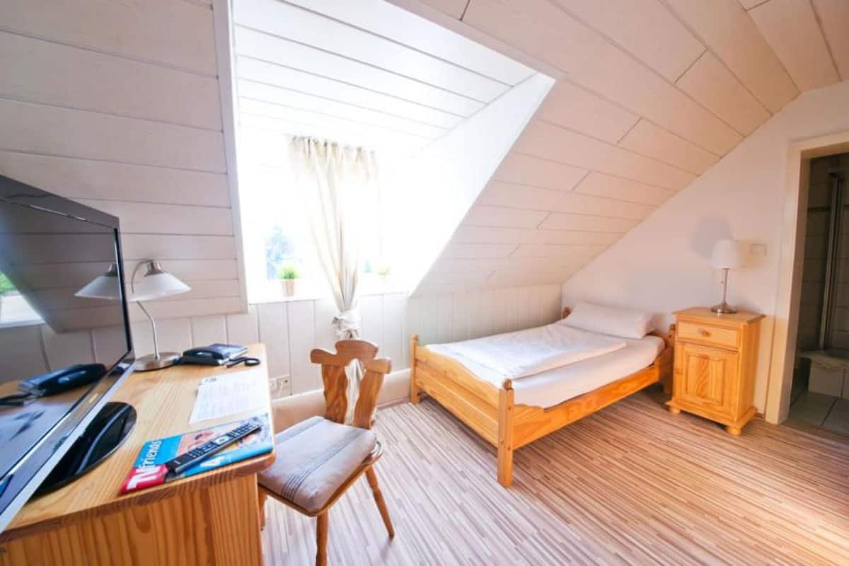 A bedroom with a sloped ceiling, a wooden bed, a desk with a computer, and a chair.