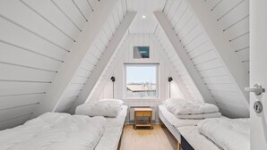 Une chambre mansardée triangulaire, avec deux lits, une petite table et une fenêtre donnant sur un paysage agréable.