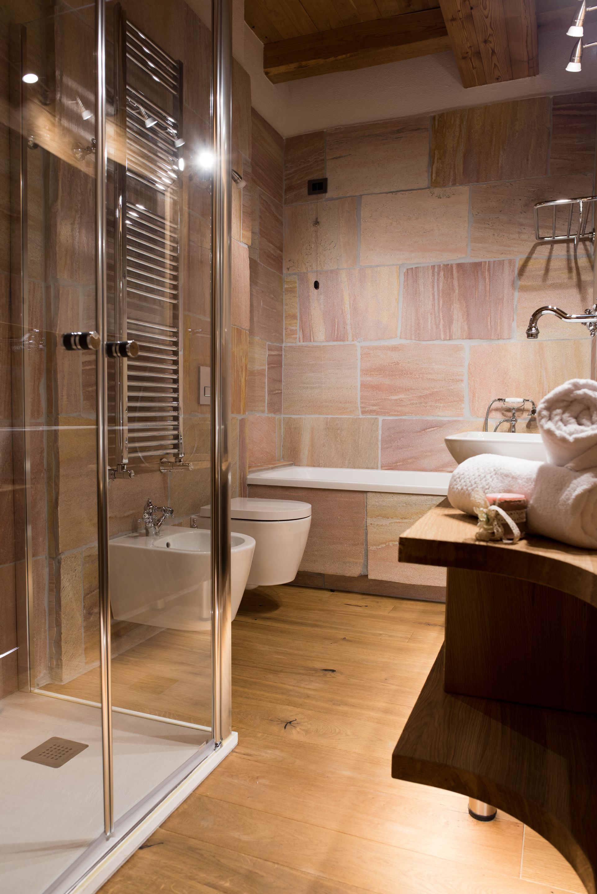 A modern bathroom with a glass shower enclosure, a wooden vanity, a bathtub, and a toilet.