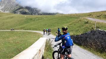 A group of cyclists on a paved path with a stone wall on one side and a grassy hill on the other.