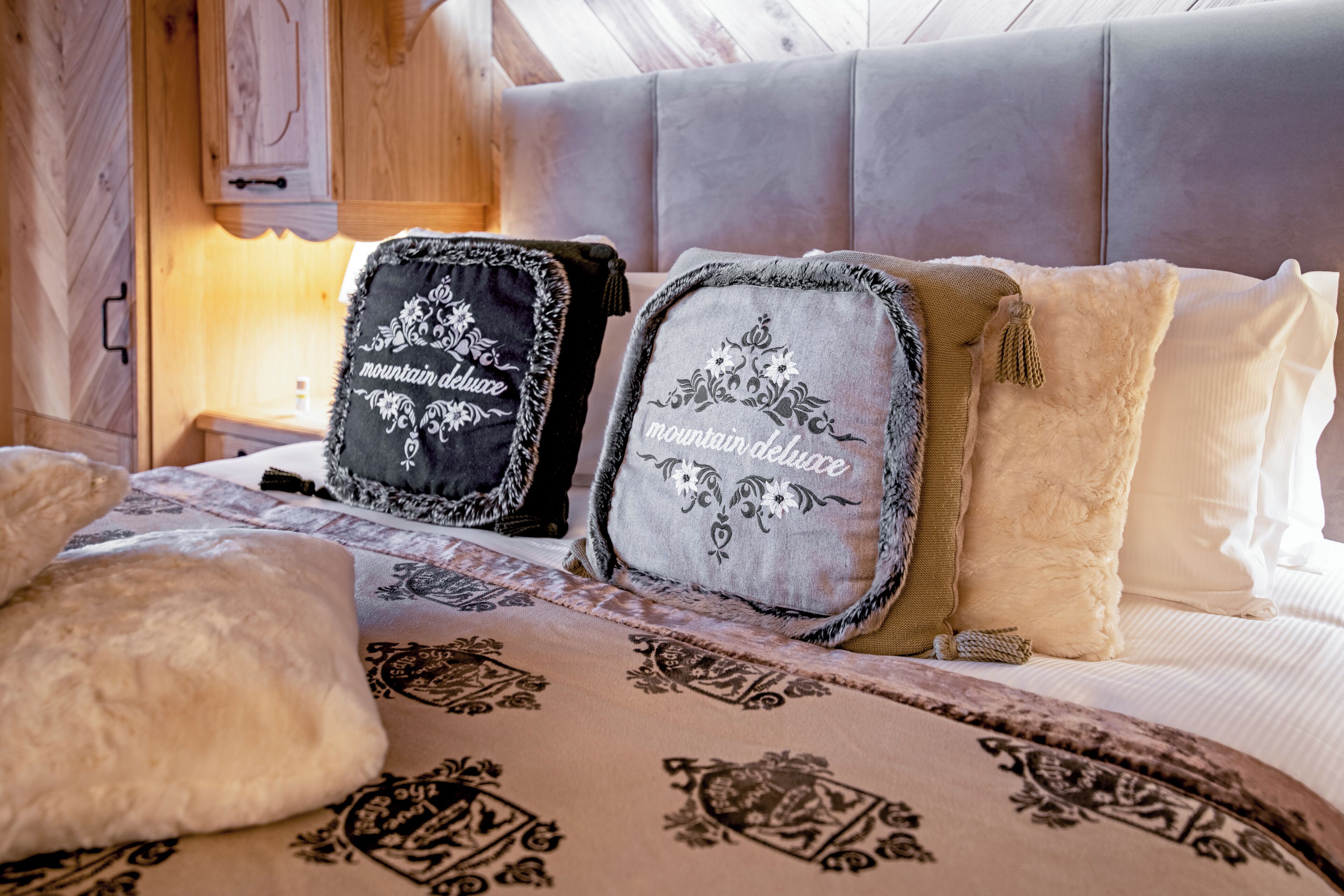 A bed with patterned bedding and two decorative pillows with embroidered text.
