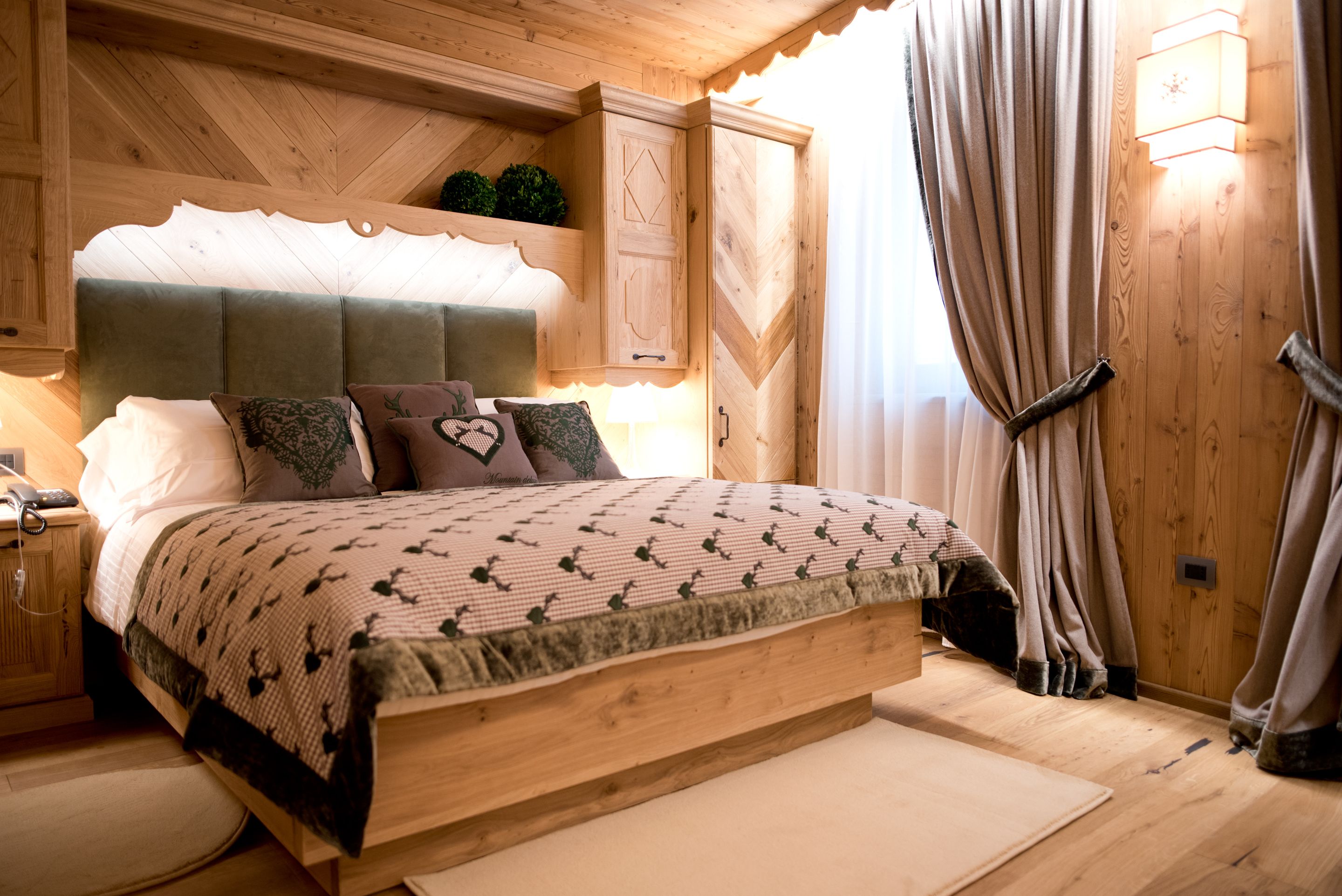 A wooden bedroom with a bed, headboard, and curtains.