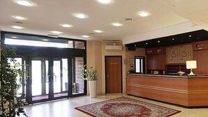 A hotel reception area with a reception desk, a large potted plant, and a red carpet. - Executive Hotel Udine (Udine)