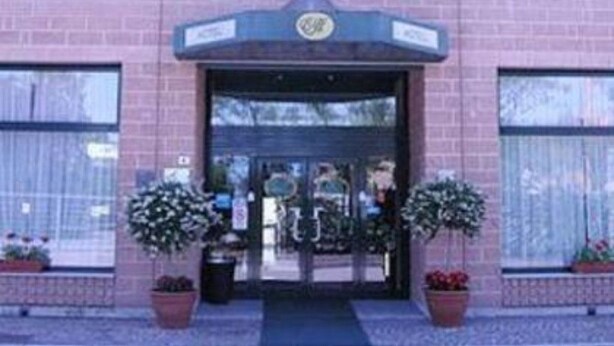 A hotel entrance with a brick facade, a glass door entrance, and multiple flags above. - Executive Hotel Udine (Udine)
