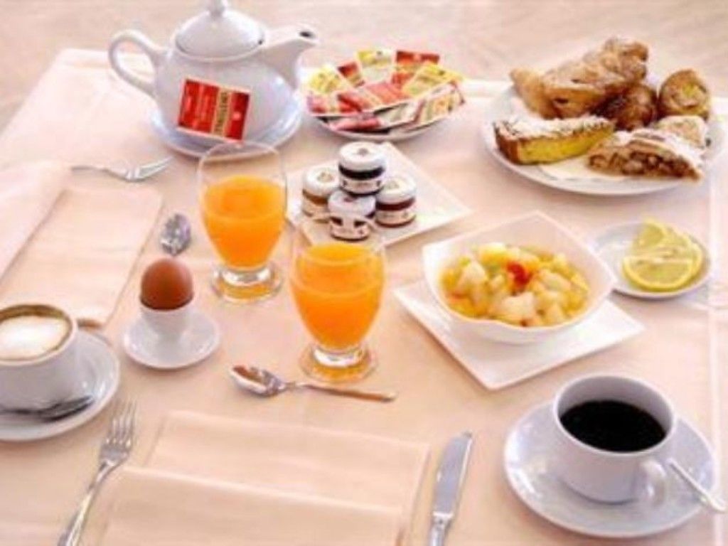 A breakfast setting with a teapot, coffee cups, orange juice, pastries, and a fruit bowl.