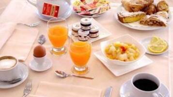 A breakfast setting with a teapot, coffee cups, orange juice, pastries, and a fruit bowl.