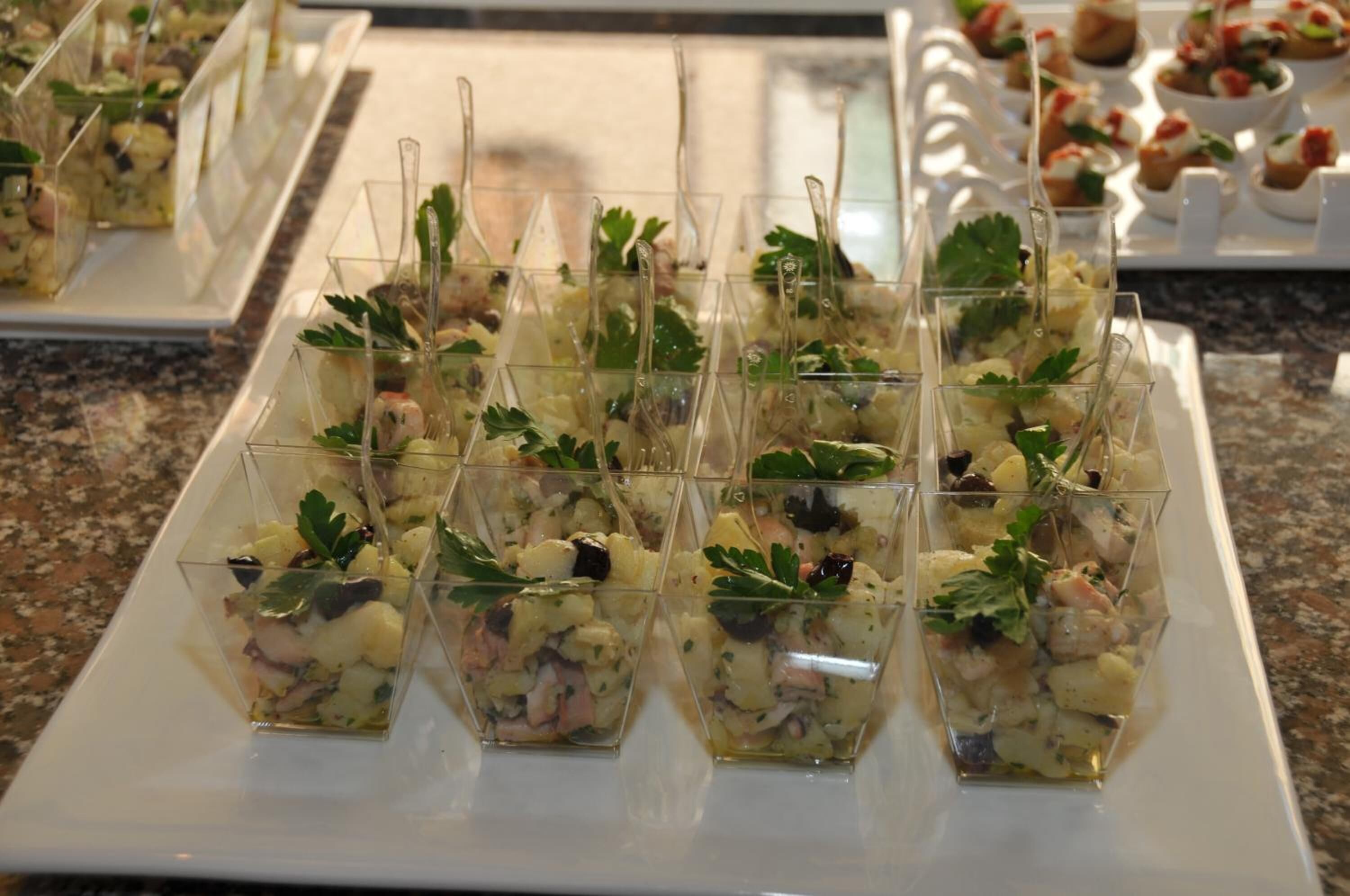 Une table de buffet avec des récipients en verre transparent remplis de nourriture, décorés de persil.