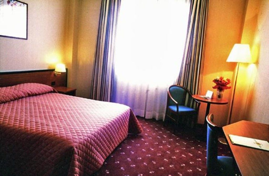 Una camera d'albergo con un letto, una sedia, un tavolino e una lampada.